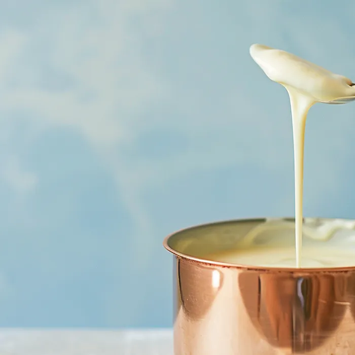 Creme de manteiga escorrendo de uma colher em panela de cobre