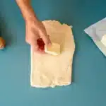Uma mão coloca manteiga num retângulo de massa aberta